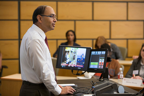 Vishal Gaur in the foreground standing behind a desk with monitors and speaking to a lecture hall of students.