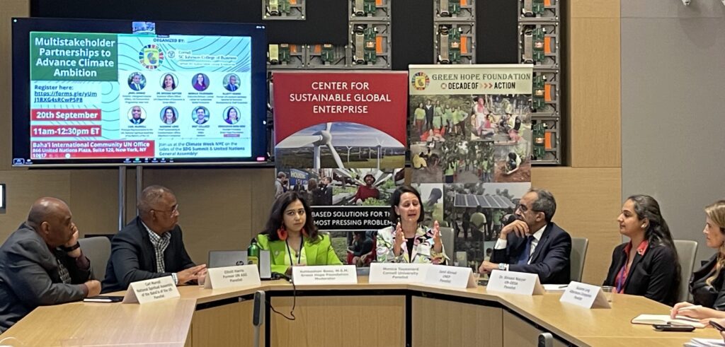 Kehkashan Basu sits at a semicircular table with six panelists. 