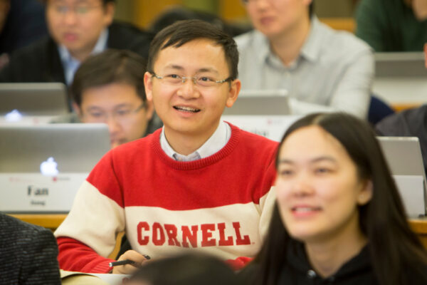 A man in a Cornell sweater sits in a tiered classroom.