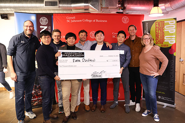 9 people standing on a stage with 5 students holding a novelty check made out to Data Don(Keys).