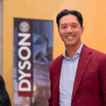 John Wu standing next to a Dyson School banner.