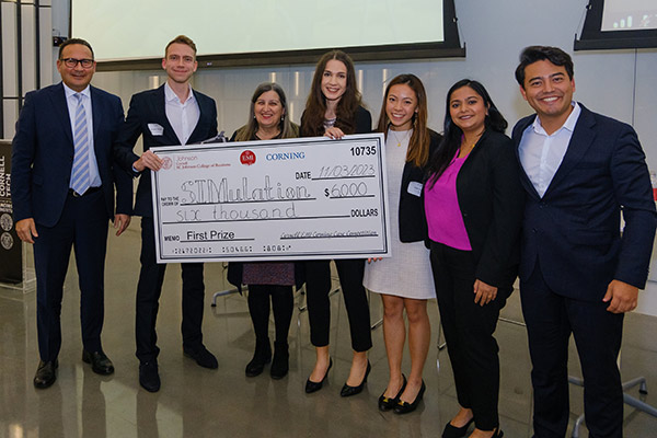 3 men and 4 women standing and holding a novelty check for $6,000 made out to SIMulation.