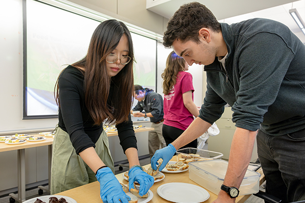Two students wearing nitrile gloves place food on plates.