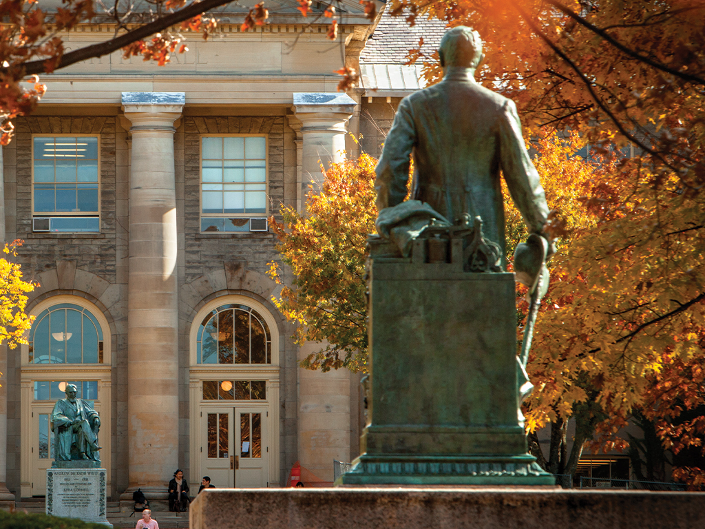 Statue of Ezra Cornell surrounded by fall foliage.