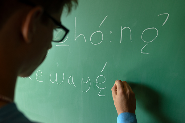 Close up of a person in glasses writing on a chalkboard