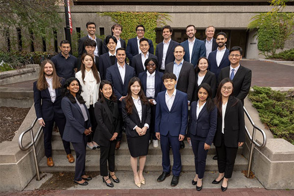 A posed group of 23 students and one faculty member dressed in business attire.