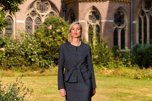 photo of Alissa Kleinnijenhuis in formal business attire standing in a garden with a older building with arched windows in the background.