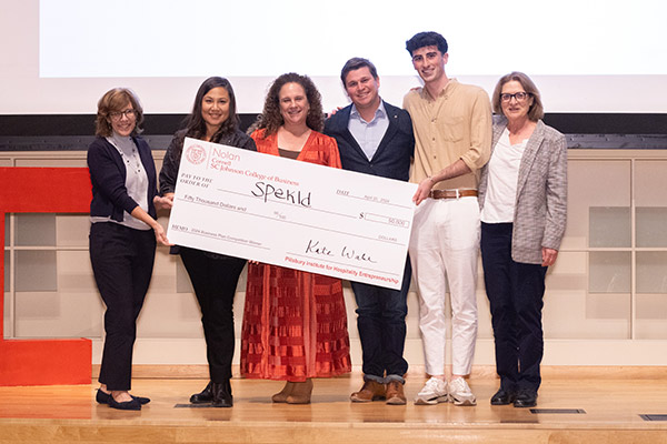 4 women and 3 men standing on a stage, smiling, and holding a novelty check for $50,000 made out to spekld.