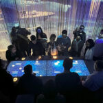 people gathered around a table lit up with large video screen display.