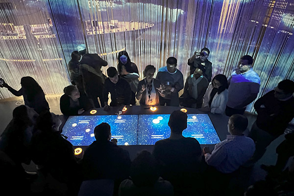 people gathered around a table lit up with large video screen display.