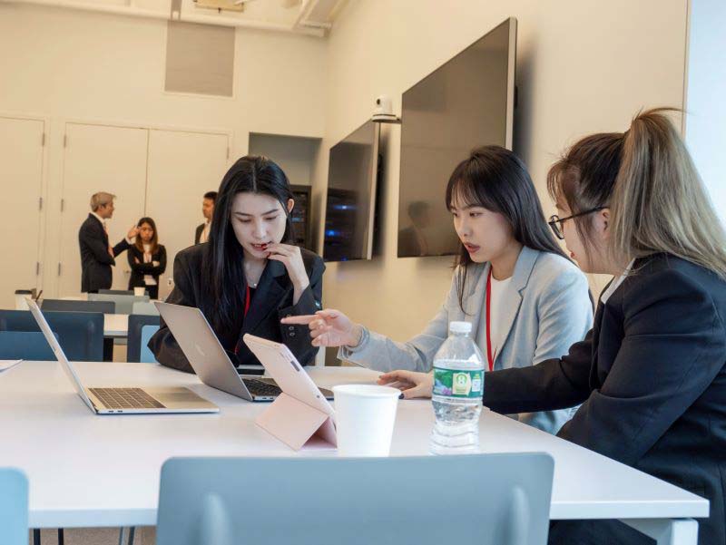 Three female students preparing for a presentation in a classroom.