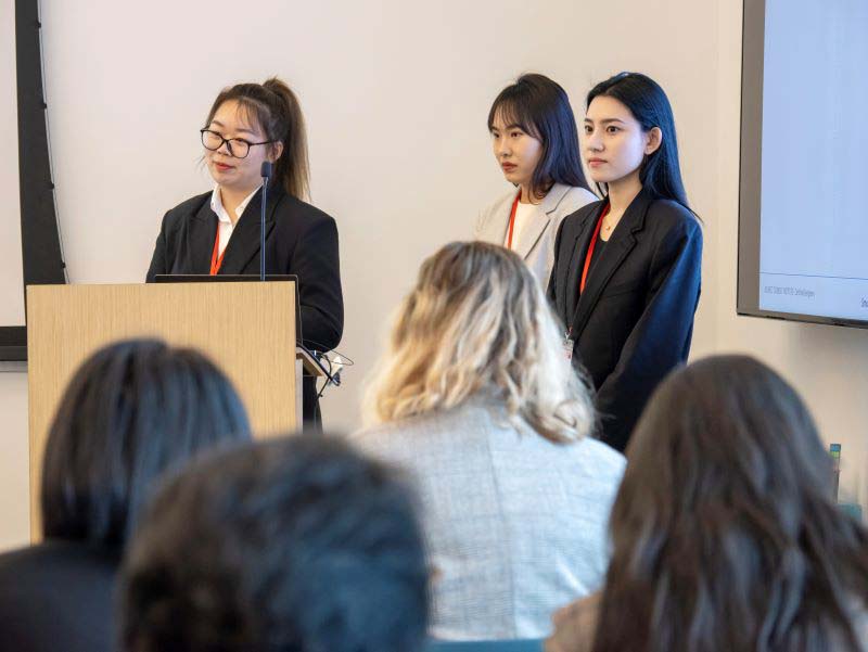 Three female students at a podium presenting in a classroom.