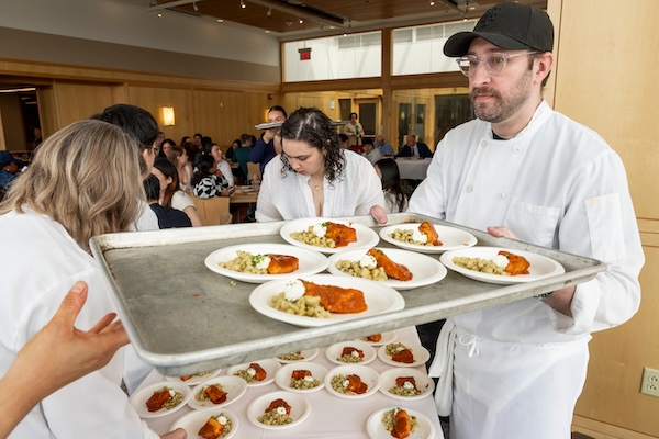 A man brings out a tray of food as students look on.