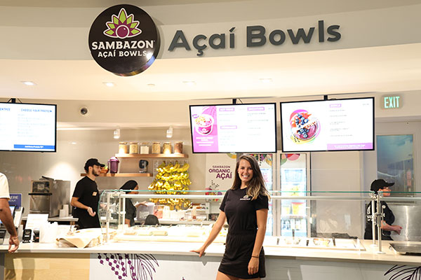 A woman standing in front of a SAMBAZON Açaí Bowls food counter.