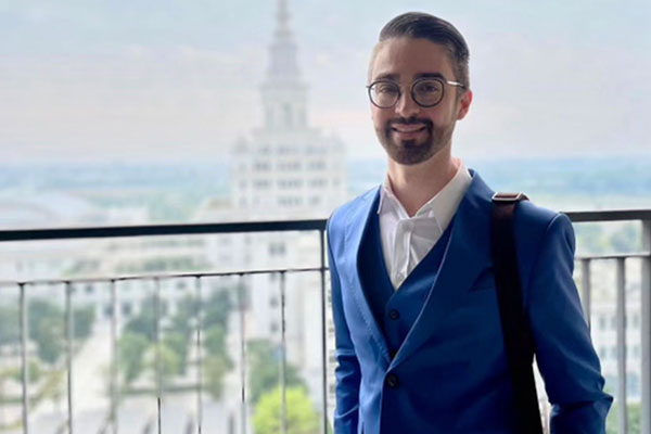 upper body shot of Andrew Foley standing on a balcony with trees and buildings in the background.