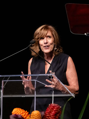 photo of Kate Walsh standing at a podium, gesturing, smiling, and speaking.