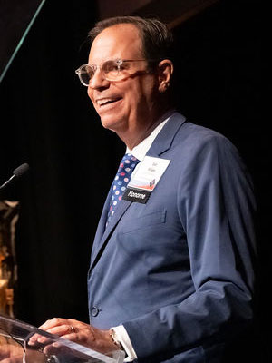 Rob Wilder standing at a podium, smiling and speaking.