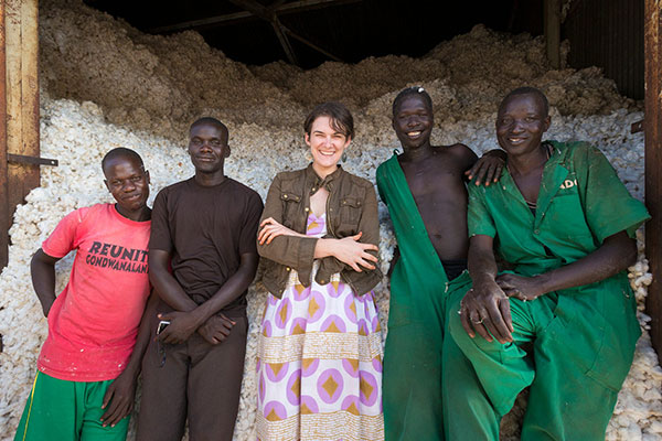 A picture of 4 Ugandan men standing next to Natalie Grillon in front of a warehouse of cotton.