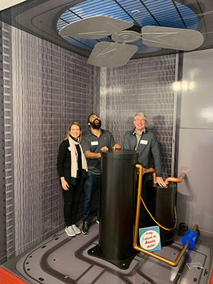 2 men and 1 woman stand surrounded by sophisticated-looking HVAC system equipment.