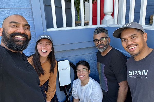 4 men and 1 woman crouched next to a compact EV charging station installed below a house porch.