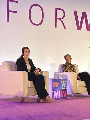 two women sitting in chairs onstage, one of them speaking.