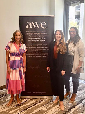 3 women standing next to a roll-up Aimbridge Women Excelling banner.