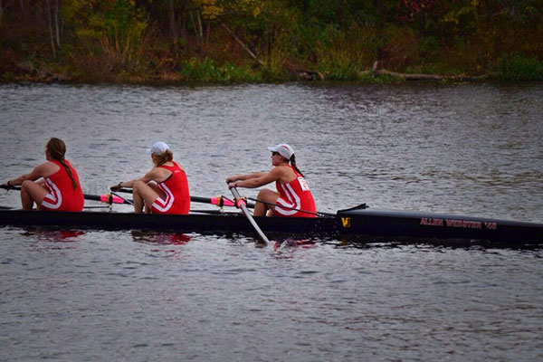 3 women, holding one oar each, rowing a long narrow boat.