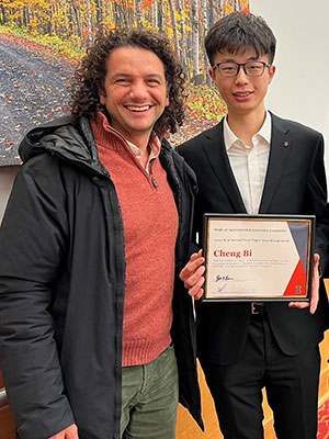 Two men standing side by side, one holding an award certificte.