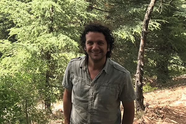 a man standing in a grove of trees dappled with sunshine and shade.