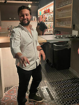 A man standing and smiling with a lit-up bar in the background.