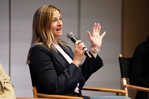 Marianne Boak in business attire sitting, gesturing with her hand, and speaking into a microphone.