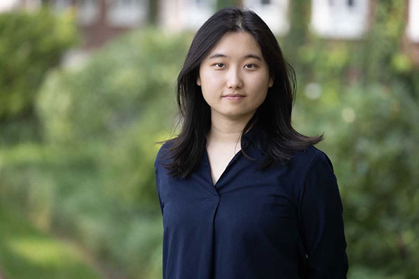 upper body enironmental photo of Yaxuan Chen with gree foliage in the background.