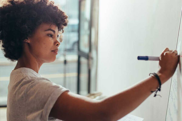 A woman stands and writes on a whiteboard.