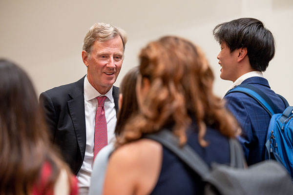 Peter Nolan in the background smiling and speaking with a group of students, whose backs are in the foreground.