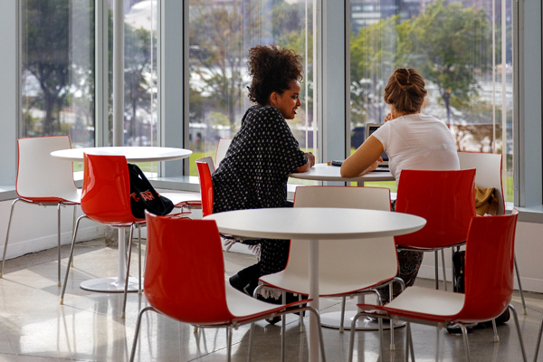 Two people sit at a round table surrounded by walls of windows.