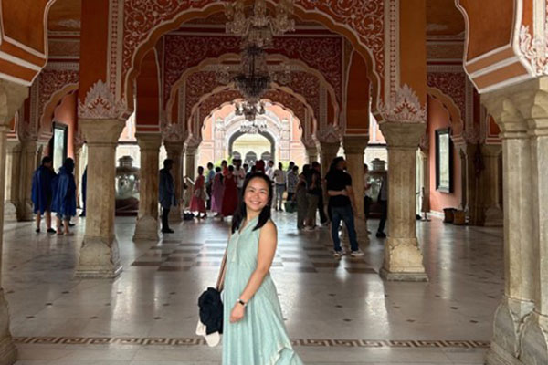 A woman standing in a latge palace surrounded by an ornate series of archways and pillars.