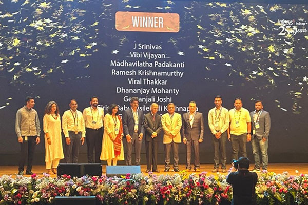 A group of 12 men and women standing on stage with a screen behind them title "winner" and a list of names.