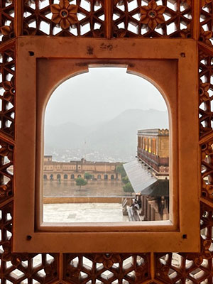 Looking out through carved wooden opening at a large courtyard and palace.