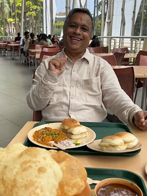 a photo of a man sitting at a table and smiling at the camera in a large restaurant with a plate of food in front of him.