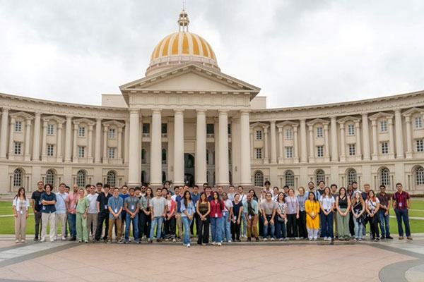 A large group of people lined up and posing for a photo in front ofo a large building with columns and a cupola.