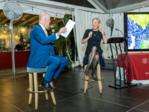 Two people in conversation holding microphones and sitting on stools.