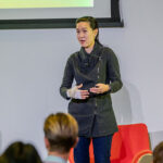 A woman on stage gesturing and speaking.