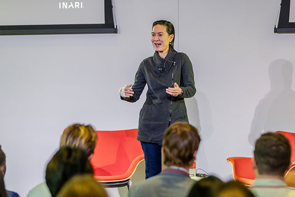 A woman standing on stage and speaking while gesturing with her hands.