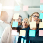 Colleagues look at post it notes on a glass board.