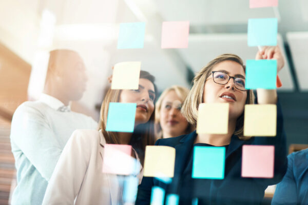 Colleagues look at post it notes on a glass board.