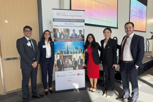 Cornell MBA students posing by an event banner