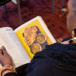 A photo of a woman looking at an open cookbook, taken from over her shoulder.