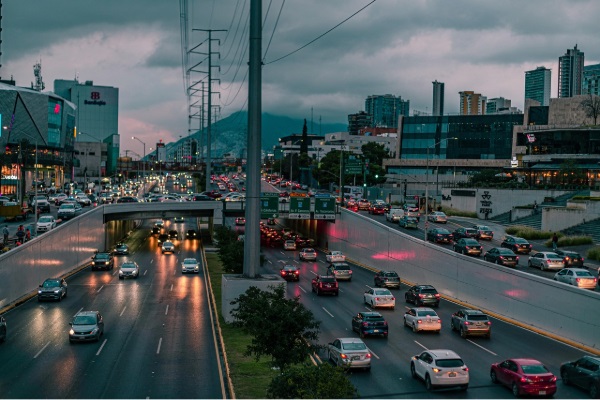 Multiple-lane roadway full of cars at dusk with a cloudy sky and a mountain in the background