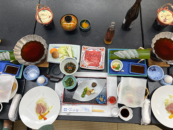 Image of a traditional kaiseki dinner featuring shabu-shabu, sashimi, various seaweeds and salads, duck, mochi, and egg