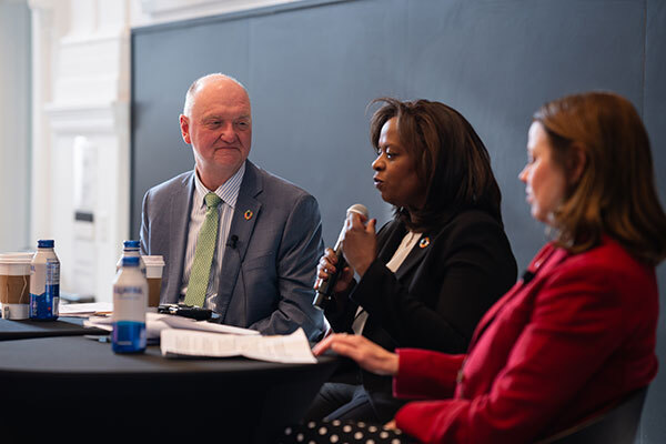 Image of a man and two women sitting at a table with a microphone